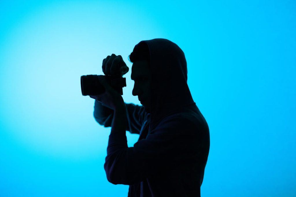 Silhouette of a photographer in a hoodie taking a photo against a blue background.